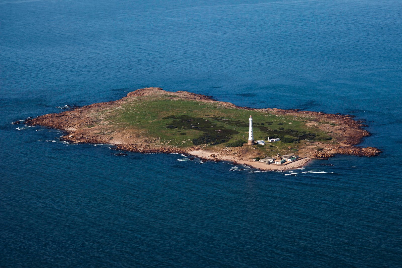 Vista aérea de la Isla de Lobos rodeada por el océano, con su faro y construcciones costeras